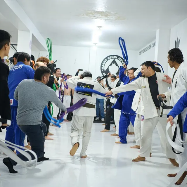 Alumnos celebran una ceremonia de graduación agitando cinturones en el pasillo del gimnasio