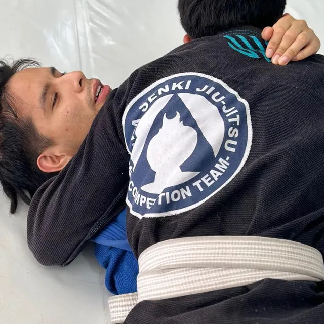 Dos practicantes de jiu-jitsu entrenando en el tatami, uno controlando desde la espalda con cinturón blanco