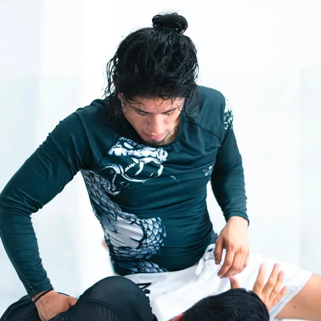 Practicante de cabello rizado controlando a un compañero en el suelo durante entrenamiento