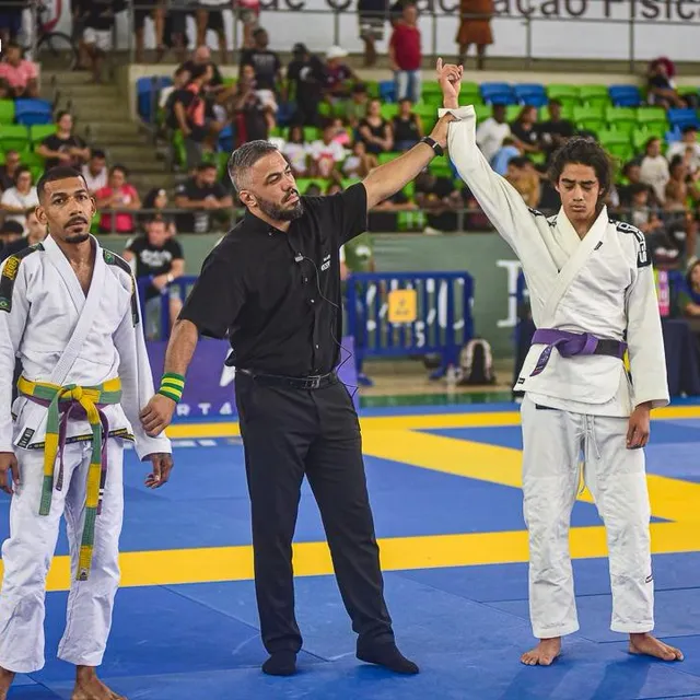 Instructor arbitrando un combate y levantando el brazo del ganador en un torneo de jiu-jitsu