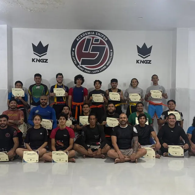 Grupo de alumnos posando con diplomas frente a un mural del gimnasio