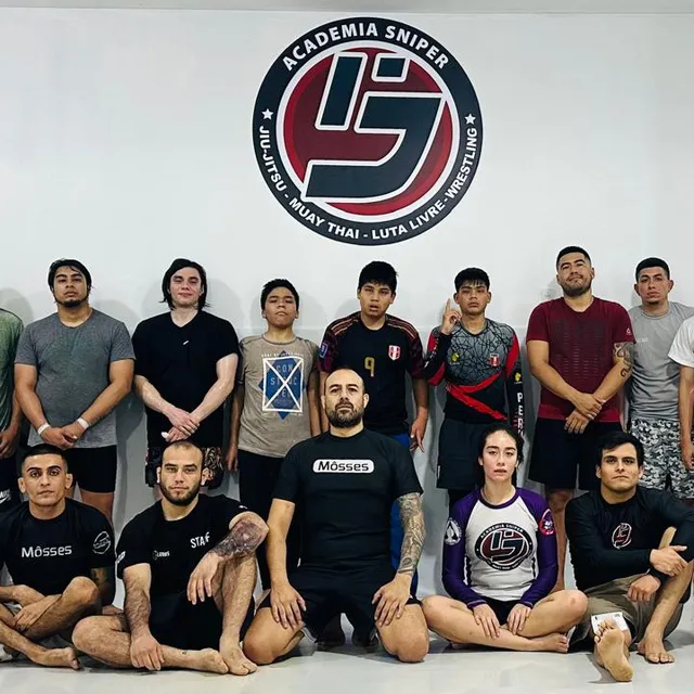 Grupo de alumnos con camisetas de colores posando frente al logo de la academia