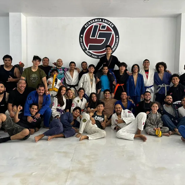 Grupo de alumnos de distintos cinturones posando frente al logo de la academia