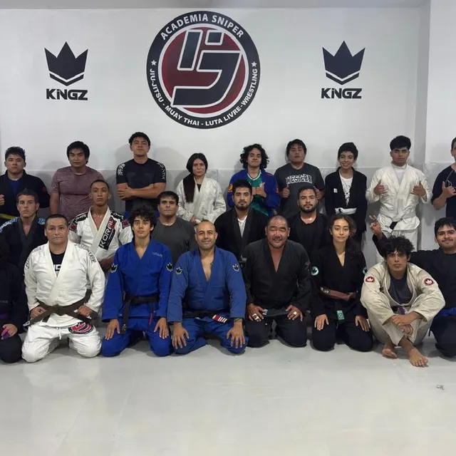 Foto grupal de alumnos en gi posando de pie y arrodillados en el gimnasio
