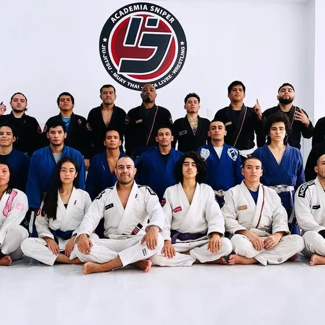 Grupo de alumnos de jiu-jitsu posando en el tatami con kimonos de distintos colores