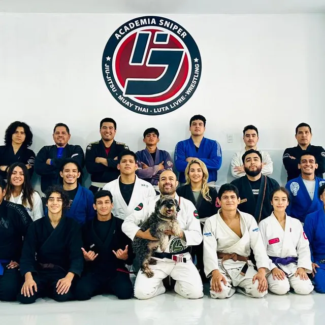 Grupo de alumnos posando junto a la mascota de la academia frente al logo de la academia