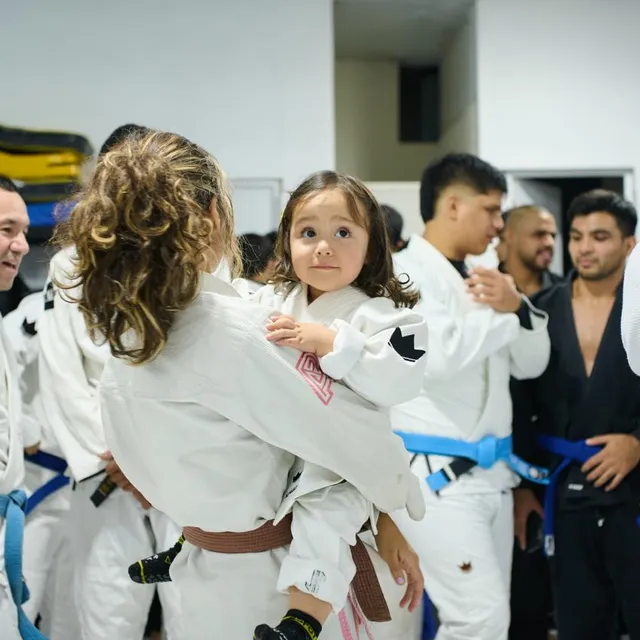 Una madre carga a una niña pequeña vestida con gi durante una reunión en la academia