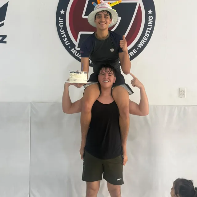 Dos alumnos celebrando un cumpleaños dentro del gimnasio, uno sobre los hombros del otro sosteniendo un pastel