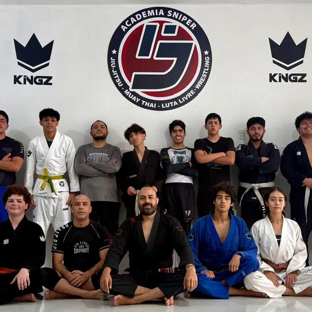 Equipo de adultos posando de pie y sentado frente al logo del gimnasio