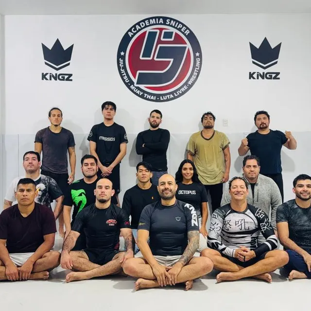 Equipo posando con ropa casual y rashguards frente al mural del gimnasio