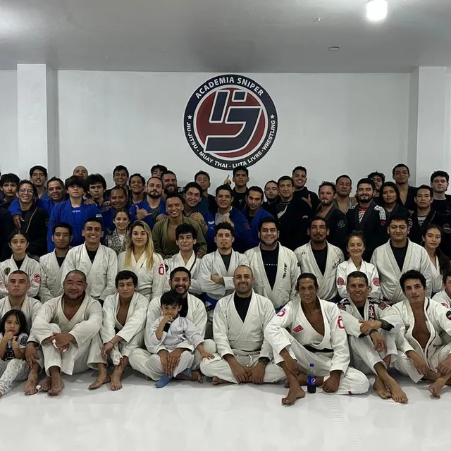 Foto grupal de todo el equipo de la academia en kimono frente al logotipo de la academia