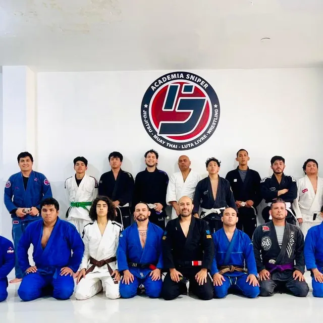 Equipo de jiu-jitsu posando en filas con gis azules y blancos frente al logo del gimnasio