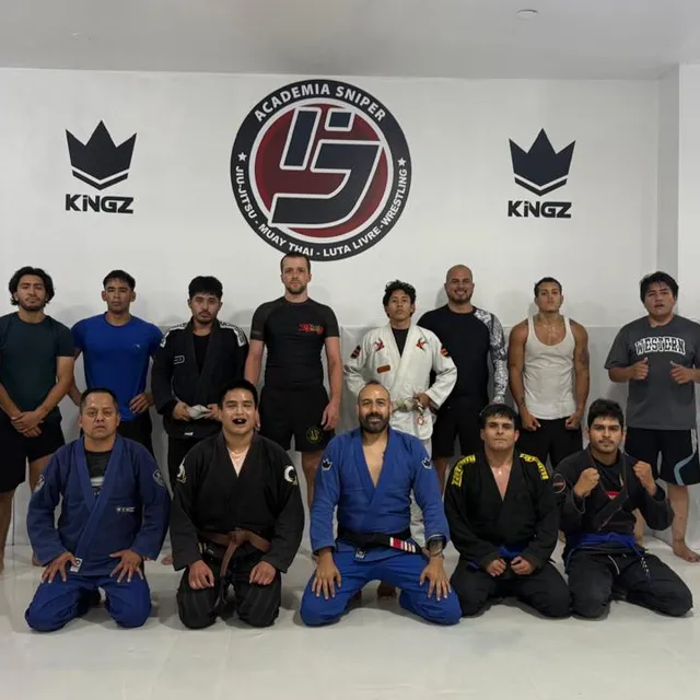 Equipo posando con gis azules y negros junto al instructor frente al logo del gimnasio