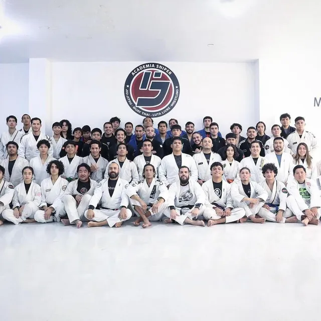 Gran fotografía grupal de alumnos de gi blanco frente al mural del gimnasio