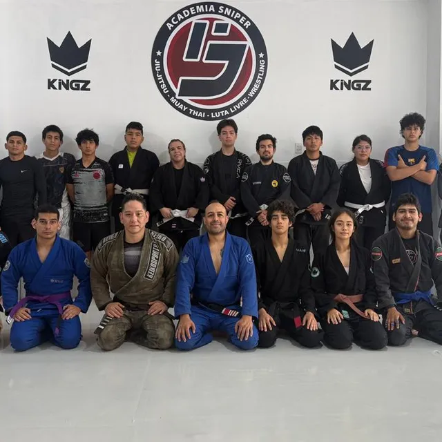 Equipo posando con el instructor frente al logo del gimnasio