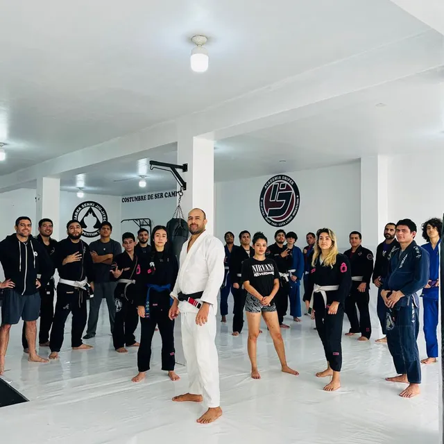 Equipo completo posando en el tatami junto al instructor, con el lema "Costumbre de ser campeón" y los logos de la academia y de Marra Senki Jiu-Jitsu pintados en la pared