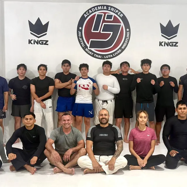 Foto grupal del equipo de alumnos vestidos de negro posando frente al logo de la academia