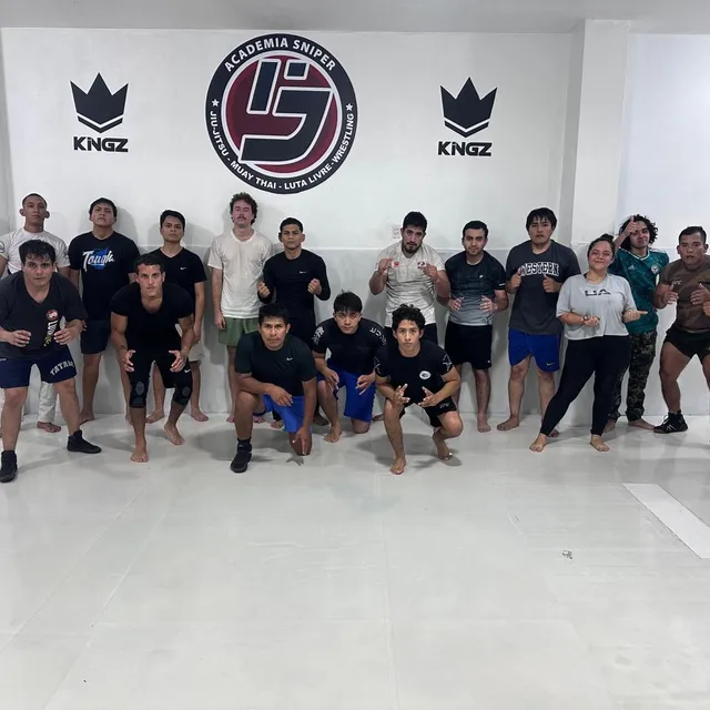 Grupo de alumnos posando de manera relajada frente al logo del gimnasio