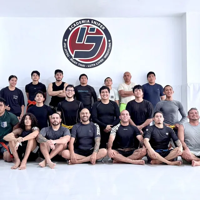 Equipo posando sentado con rashguards negros frente al logo de la academia