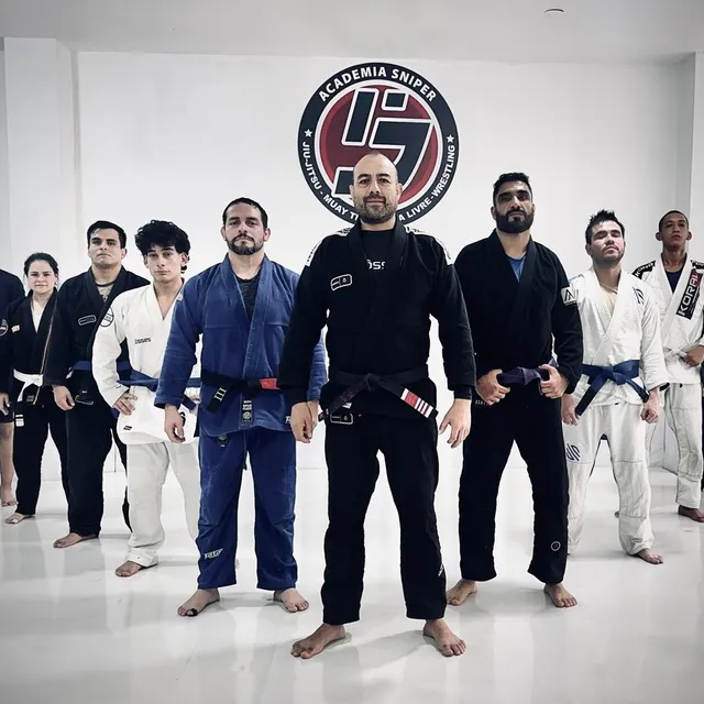 Instructor posando al frente de un grupo de alumnos frente al logo de la academia