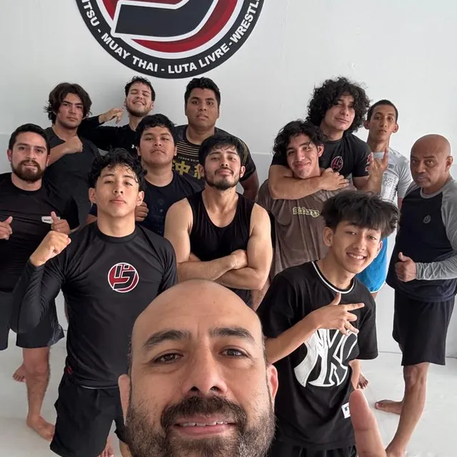 Selfie grupal del instructor con alumnos jóvenes frente al logo de la academia