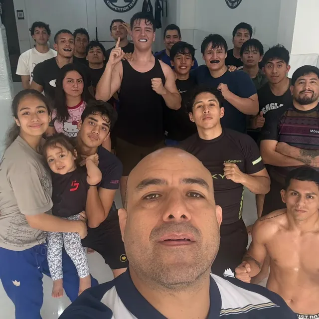 Selfie grupal del equipo en el gimnasio con un instructor en primer plano y alumnos sonriendo detrás