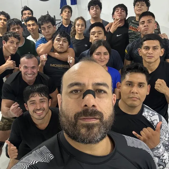 Selfie grupal de un entrenador con el equipo de competencia, sonriendo y haciendo señas de shaka