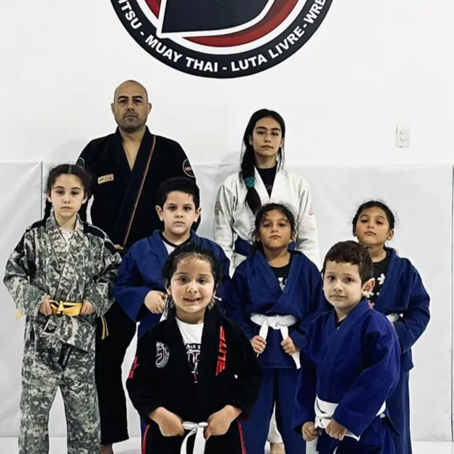 Niños de la clase infantil posando con sus kimonos junto a un instructor frente al logo de la academia