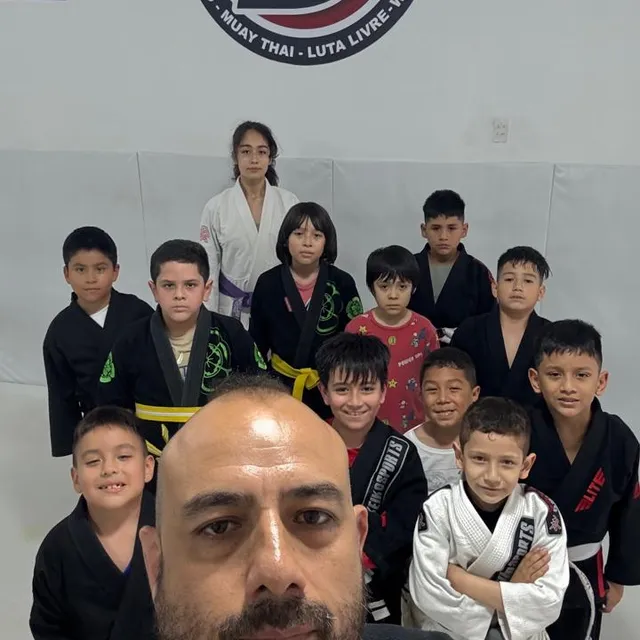 Instructor con barba en selfie junto a un grupo de niños en clase de jiu-jitsu