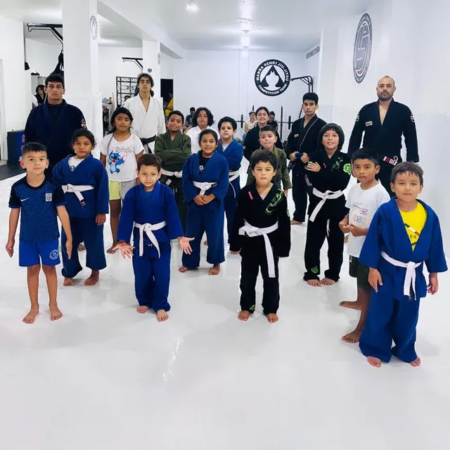 Grupo de niños de la clase de jiu-jitsu formados en el pasillo del gimnasio junto a sus instructores
