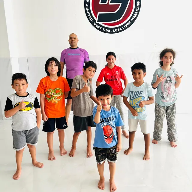 Niños de la clase infantil posando con su instructor frente al logo de la academia