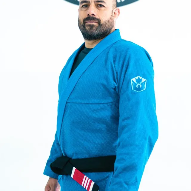 Primer plano del instructor con barba y gi azul frente al logo del gimnasio